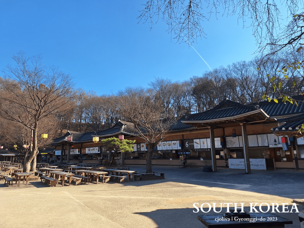 Traditional Korean food court with tiled-roof stalls, picnic tables, and festive lanterns at Korean Folk Village in Gyeonggi-do, South Korea, 2023