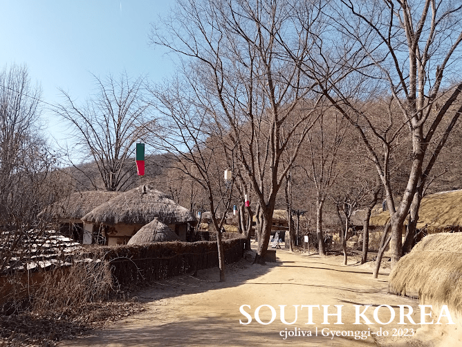 Traditional Korean village pathway with thatched-roof houses, leafless trees, and colorful lanterns in Gyeonggi-do, South Korea, 2023