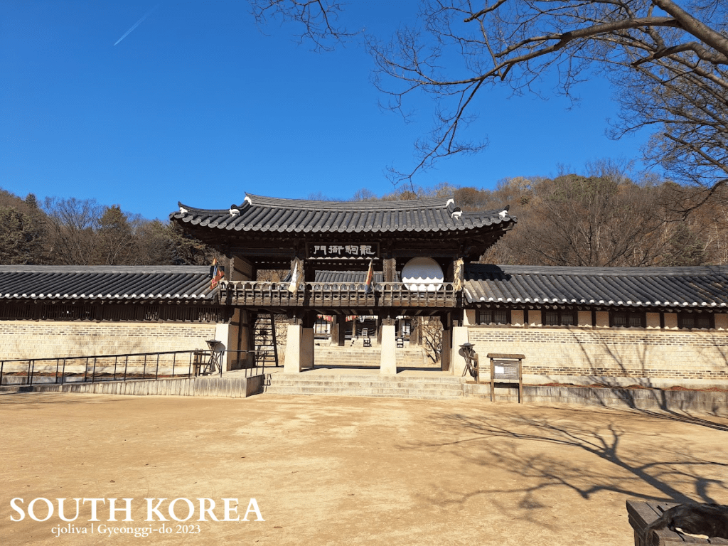 Traditional Korean gate with tiled roof, stone walls, and flags at Korean Folk Village in Gyeonggi-do, South Korea, 2023