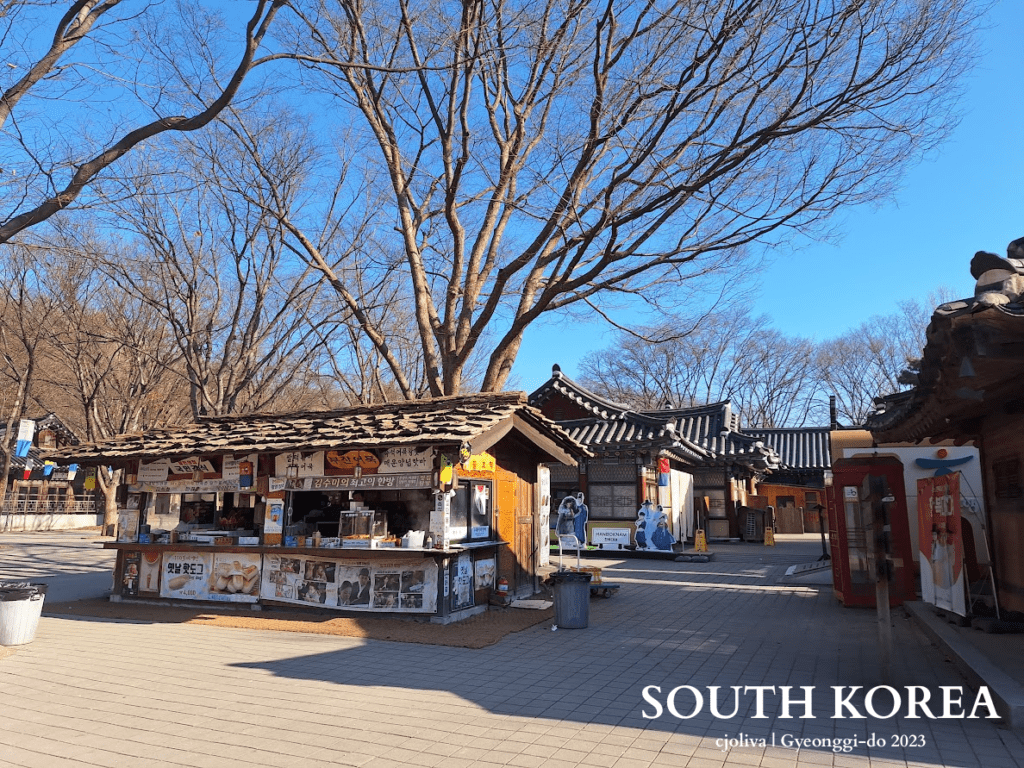 Traditional Korean street scene with food stall, cultural cutouts, and tiled-roof architecture at Korean Folk Village in Gyeonggi-do, South Korea, 2023