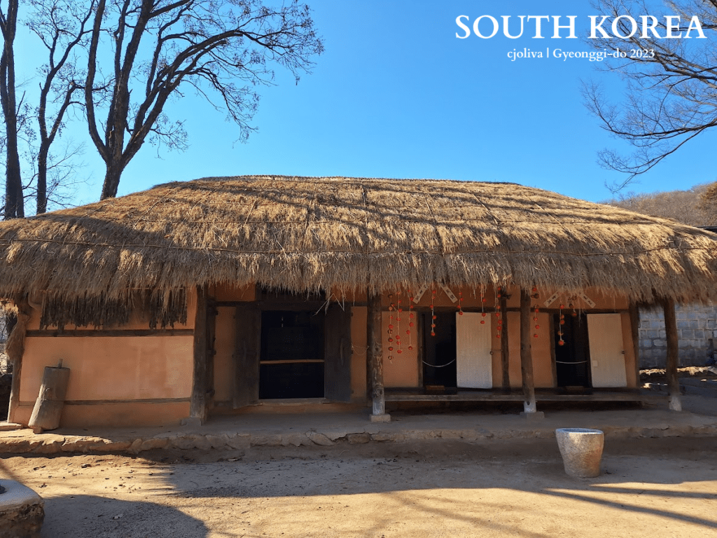 Traditional Korean thatched-roof hanok with festive red decorations and leaf bundles under eaves at Korean Folk Village in Gyeonggi-do, South Korea, 2023