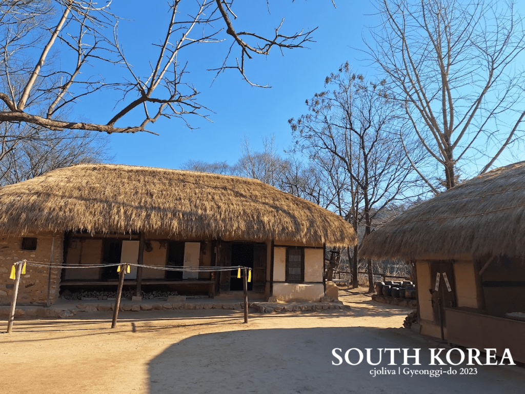 Thatched-roof traditional Korean house with rope barrier and leafless trees at Korean Folk Village in Gyeonggi-do, South Korea, 2023