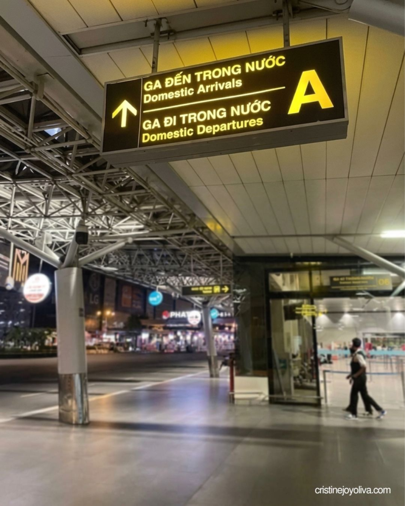 An illuminated black directional sign reading "Domestic Arrivals" and "Domestic Departures" at Tan Son Nhat International Airport in Ho Chi Minh City.