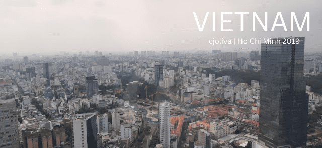 Panoramic view of Ho Chi Minh City, Vietnam, showing a dense urban landscape with high‑rise buildings, residential structures, modern and older architecture, and a tall dark skyscraper under an overcast sky.