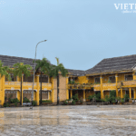 Vibrant yellow colonial buildings in Hoi An Ancient Town, Vietnam, after rain, with a wet courtyard, palms, and blue sky.
