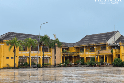 Vibrant yellow colonial buildings in Hoi An Ancient Town, Vietnam, after rain, with a wet courtyard, palms, and blue sky.