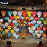 Colorful illuminated lanterns hanging in front of a shop in Hội An, Vietnam, with stools, baskets, and a wooden chair in the market setting.