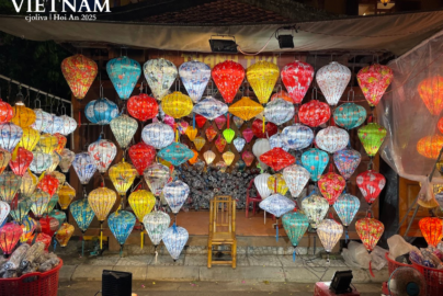 Colorful illuminated lanterns hanging in front of a shop in Hội An, Vietnam, with stools, baskets, and a wooden chair in the market setting.