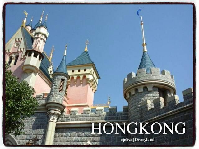 Fairy tale castle at Hong Kong Disneyland with stone walls, golden spires, and conical blue roofs under a clear sky.