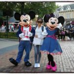 Visitors posing with Mickey Mouse and Minnie Mouse at Hong Kong Disneyland, with casual outfits, smiles, and the Disneyland Emporium in the background.