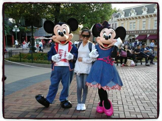 Visitors posing with Mickey Mouse and Minnie Mouse at Hong Kong Disneyland, with casual outfits, smiles, and the Disneyland Emporium in the background.