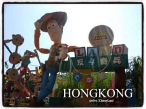 A large Woody statue tipping his hat at the entrance to Toy Story Land in Hong Kong Disneyland, with colorful oversized toys and playful decorations.