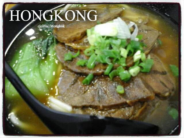 Bowl of Hong Kong Mongkok beef noodle soup with braised beef slices, bok choy, chopped green onions, and dark broth.