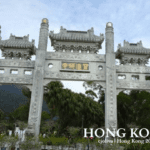 Traditional Chinese stone archway with ornate carvings and roofs at the entrance to Po Lin Monastery in Hong Kong, surrounded by trees and mountains.