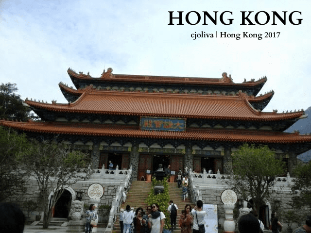 Po Lin Monastery in Hong Kong with an ornate multi-tiered roof, decorative carvings, and visitors ascending the staircase.