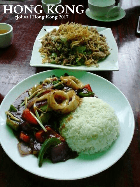 A plate of white rice with squid stir-fry, bell peppers, onions, and vegetables in dark sauce, alongside a noodle dish topped with shredded garnish at a Hong Kong restaurant.