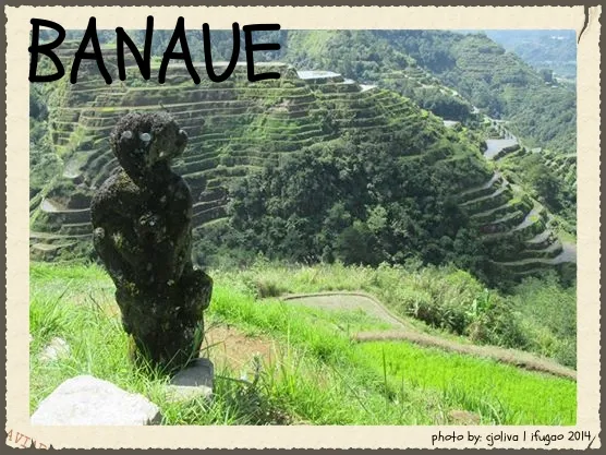A dark, carved wooden Bulul statue standing in the foreground, overlooking the lush green stepped rice terraces of Banaue, Ifugao.