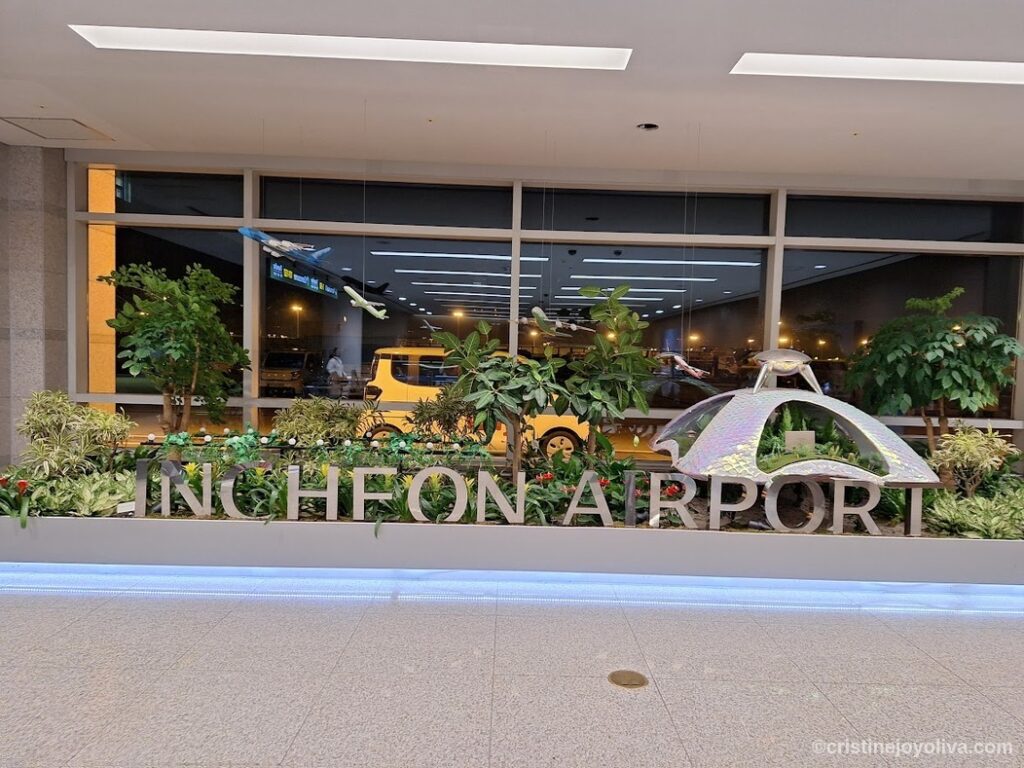 Decorative garden display with plants, model airplanes, and metallic Incheon Airport letters inside terminal