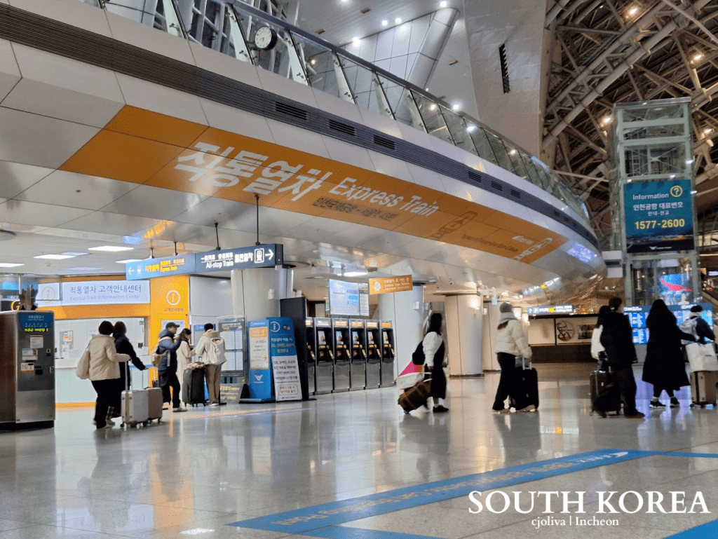 Interior view of the Incheon Airport Express Train (AREX) station featuring ticket kiosks and travelers with luggage.