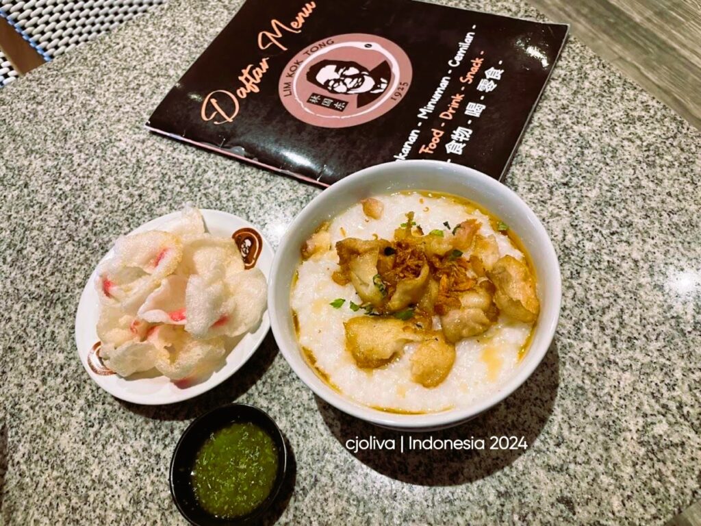 Indonesian bubur ikan rice porridge topped with fried shallots, herbs, and crispy fish, served with prawn crackers and sambal at Lim Kok Tong restaurant