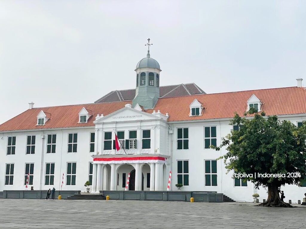 The white colonial-style Jakarta History Museum building with a red-tiled roof and bell tower under a clear sky in Fatahillah Square.