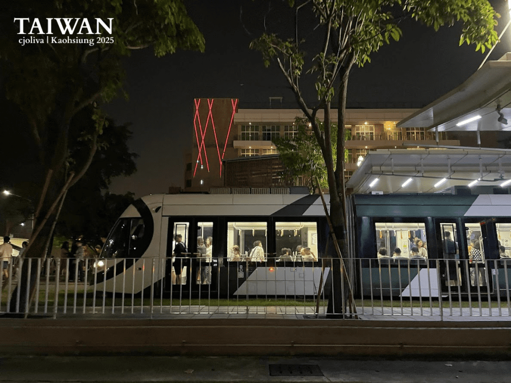 Side profile of a modern green and white Kaohsiung Light Rail (LRT) train at a station at night, with passengers visible through the lit windows.