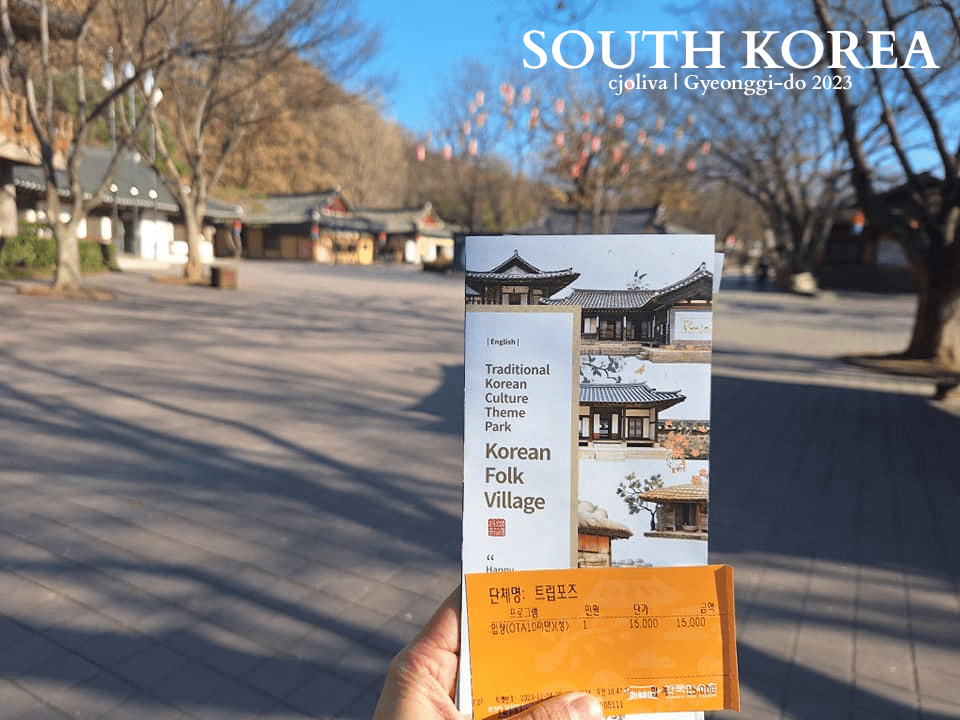 Visitor holding admission ticket and brochure at Korean Folk Village entrance with traditional Korean architecture in Gyeonggi-do