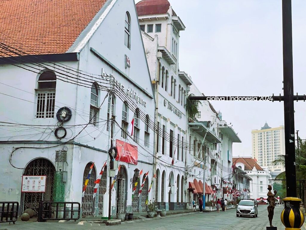 A street view of white Dutch colonial buildings with arched windows and red tiled roofs in the Kota Tua district of Jakarta.