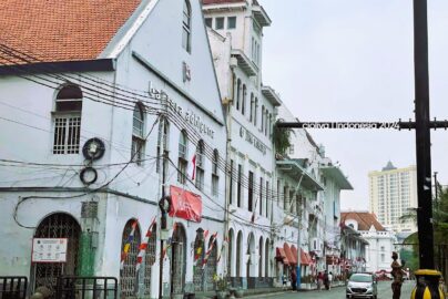 A street view of white Dutch colonial buildings with arched windows and red tiled roofs in the Kota Tua district of Jakarta.