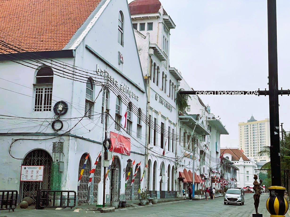 A street view of white Dutch colonial buildings with arched windows and red tiled roofs in the Kota Tua district of Jakarta.