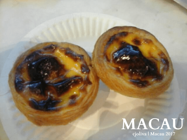 Two Portuguese egg tarts on a white paper plate with flaky golden crust and caramelized custard filling, photographed on a marble surface.
