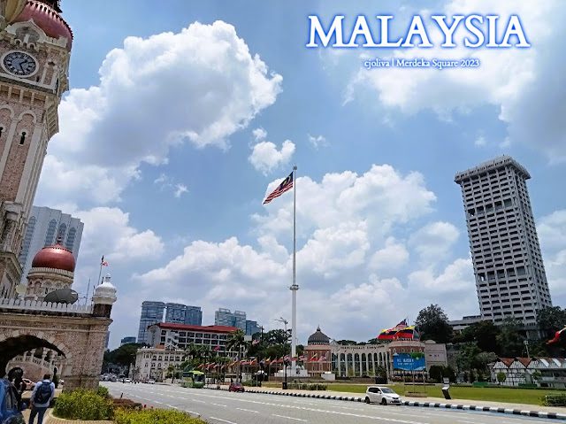 Merdeka Square in Kuala Lumpur, Malaysia, with the tall flagpole flying the national flag, Sultan Abdul Samad Building, and surrounding colonial and modern architecture.