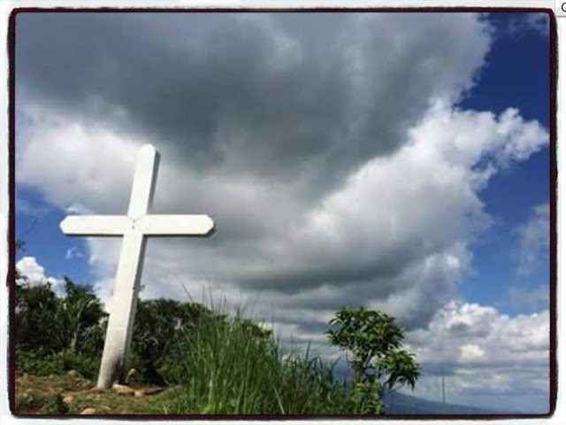 White cross at Mt. Manabu summit in Batangas surrounded by grass and dramatic sky