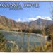 A panoramic view of Nagsasa Cove in Zambales, Philippines, featuring a crescent-shaped beach, clear blue water, and brown mountains under a bright sky, framed by dry reeds.