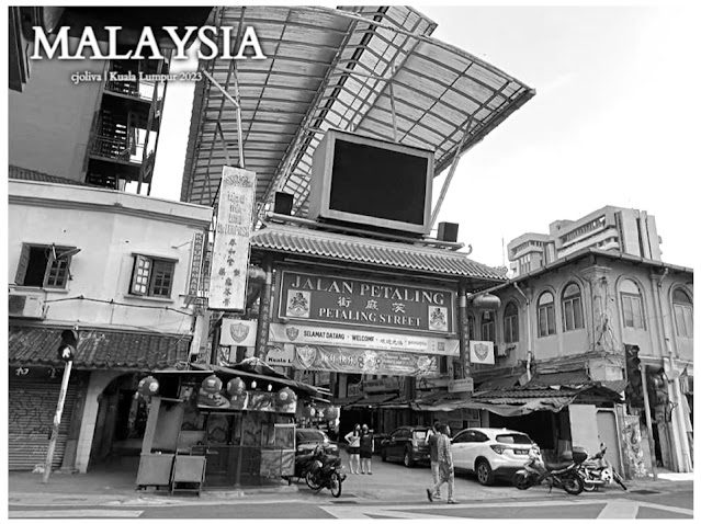 Entrance to Petaling Street in Kuala Lumpur, Malaysia, with a traditional Chinese archway, multilingual welcome signs, bustling shops, and a modern canopy structure.