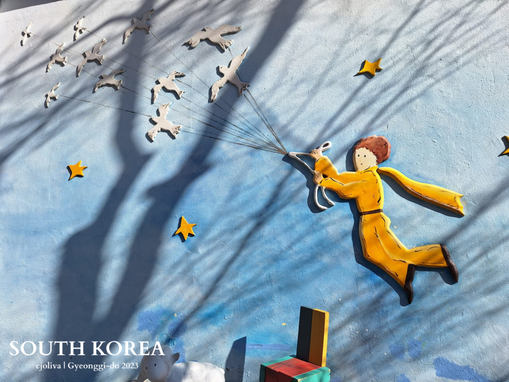 Little Prince mural in Petite France, Gyeonggi-do, South Korea, showing the character holding strings attached to flying birds with stars in the background.