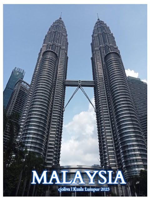 The Petronas Twin Towers in Kuala Lumpur, Malaysia, viewed from below with the skybridge and Islamic-inspired geometric design against a partly cloudy sky.