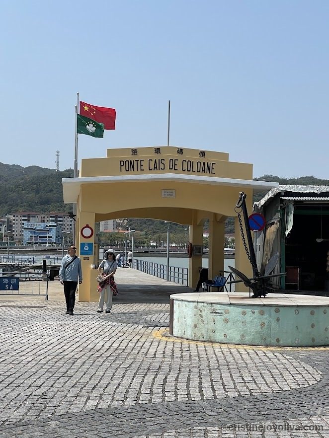 Entrance to Ponte Cais de Coloane pier in Macau with Portuguese and Chinese signage, flags, and waterfront view