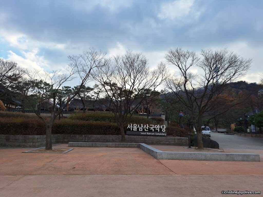 Entrance area of Seoul Namsan Gugakdang with a traditional Korean building, tiled roof, and leafless trees in late autumn.