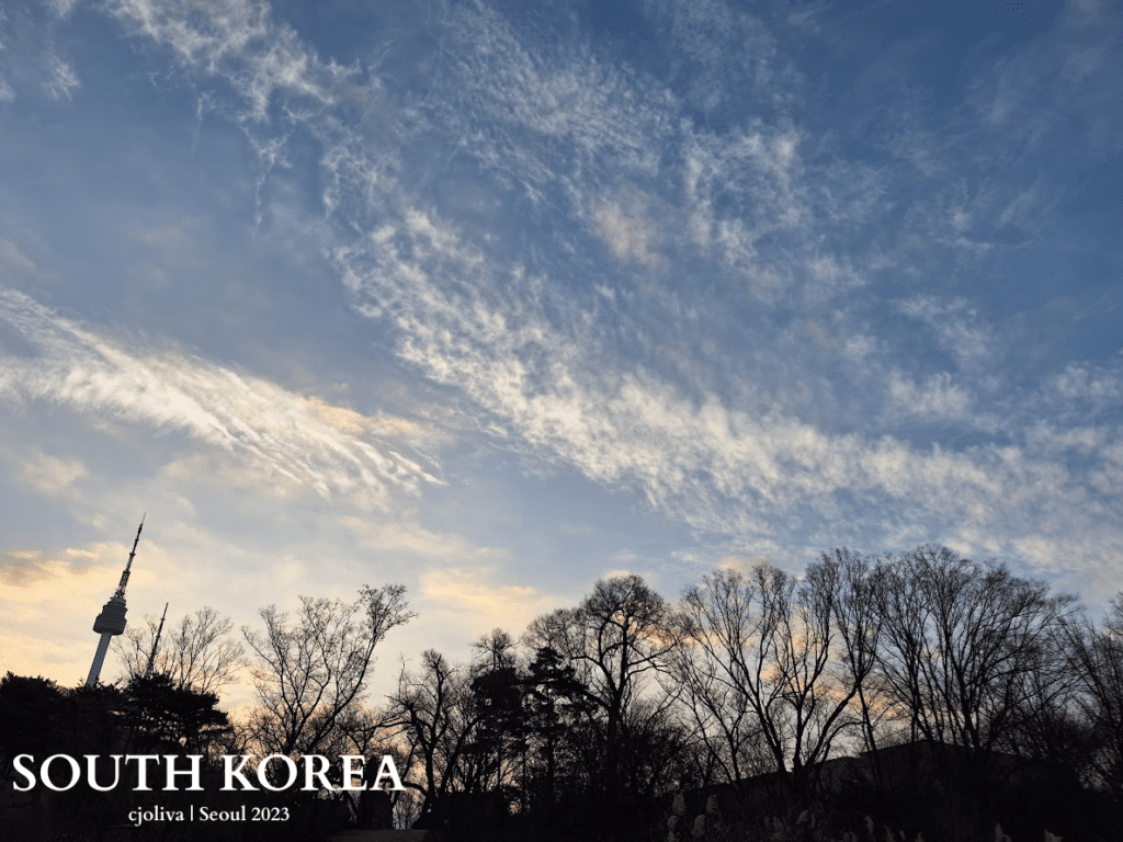Namsan Seoul Tower silhouetted against a colorful sunrise sky with wispy clouds and bare trees in Seoul, South Korea.
