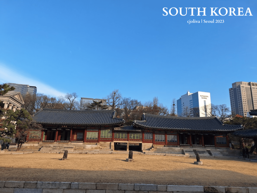 Traditional Korean palace building with tiled roof and wooden architecture in Seoul, South Korea, set against modern skyscrapers, including the Koreana Hotel.