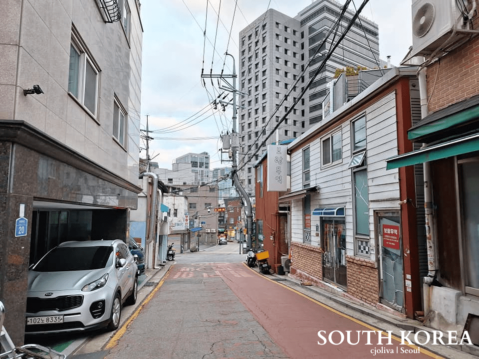 A narrow, clean Seoul side street with mixed modern and traditional brick buildings under a cloudy sky.
