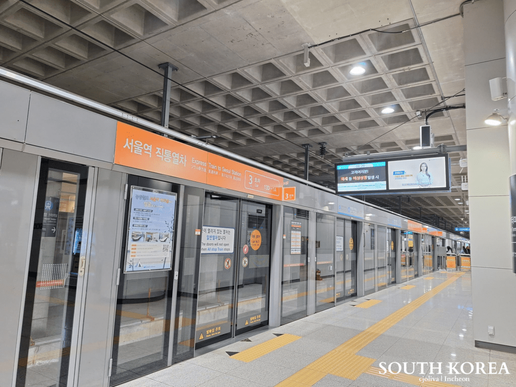 A modern, minimalist train platform at Seoul Station featuring glass safety doors and orange signage for the Airport Express Train.
