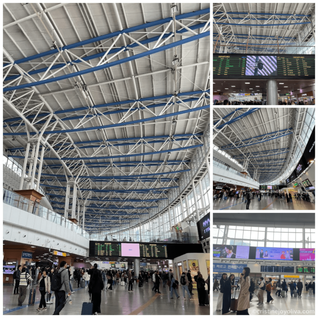 Interior of Seoul Station with curved steel ceiling, digital departure boards, travelers with luggage, and natural light from large windows