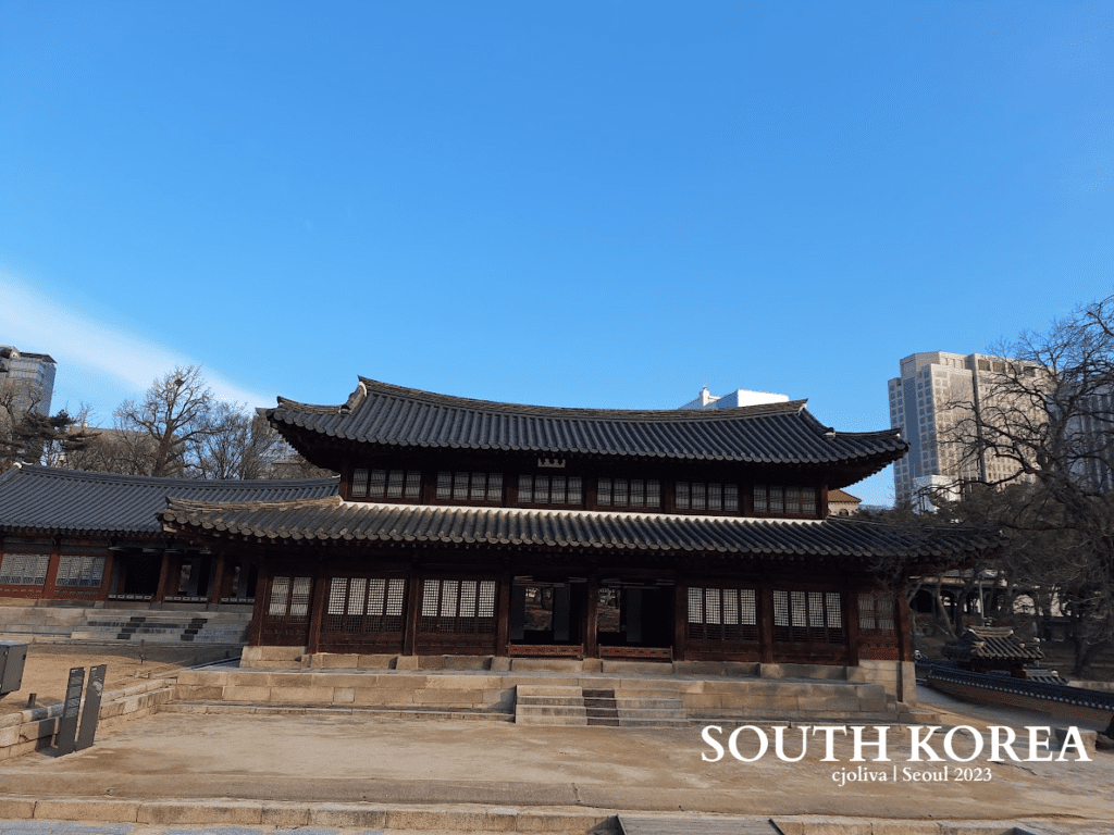 Traditional Korean palace with wooden architecture and tiled roofs in Seoul, South Korea, contrasted against modern high-rise buildings, including the Koreana Hotel.