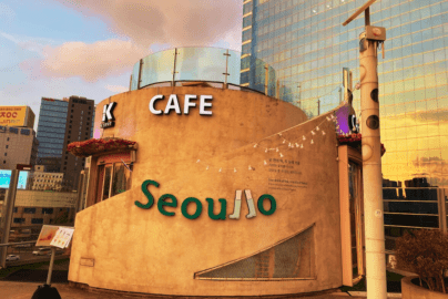 The exterior of K-Cafe on the Seoullo 7017 elevated walkway during sunset, with the golden light reflecting off a modern glass skyscraper in the background.