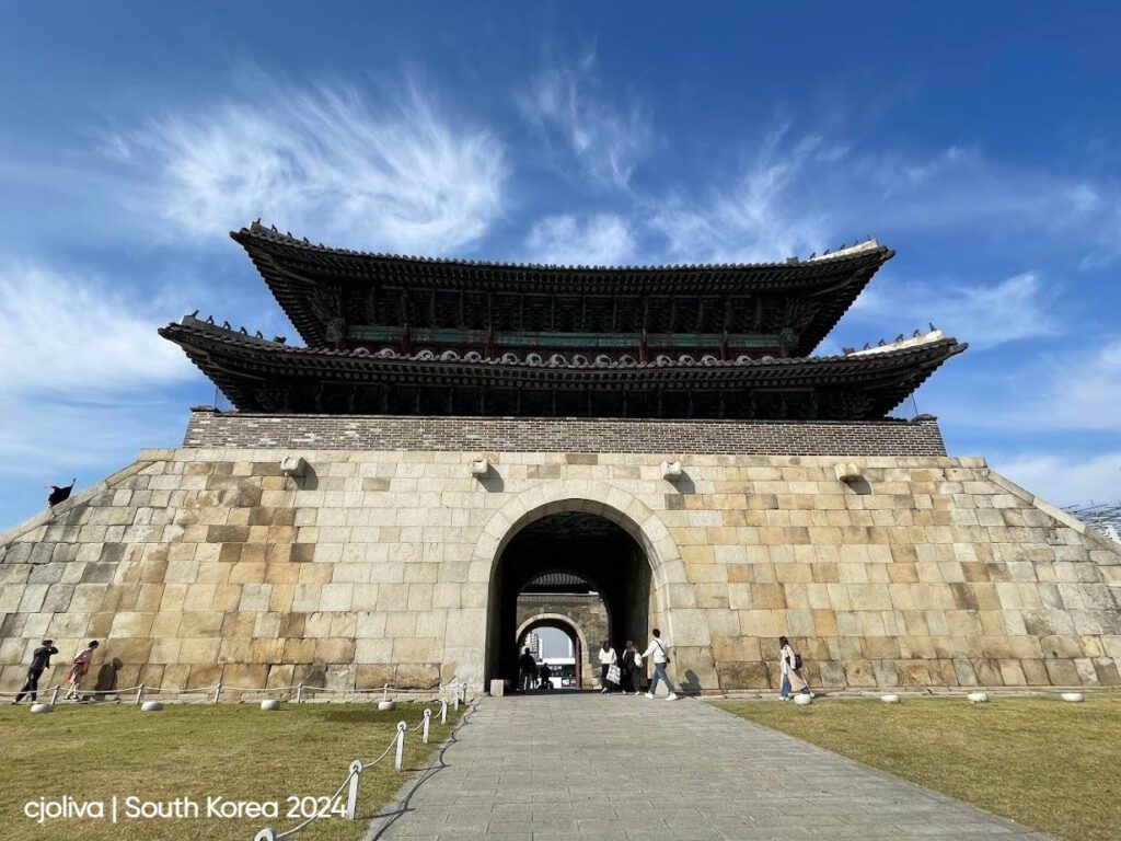 Hwaseong Fortress gate in Suwon, South Korea, with a stone base, an arched entrance, and a two-tiered wooden pavilion featuring ornate eaves and colorful detailing.