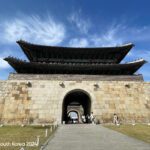Hwaseong Fortress gate in Suwon, South Korea, with a stone base, an arched entrance, and a two-tiered wooden pavilion featuring ornate eaves and colorful detailing.