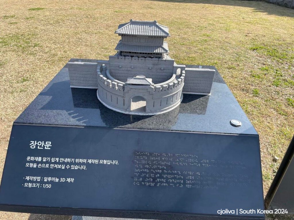 Miniature tactile model of Janganmun Gate at Hwaseong Fortress in Suwon, South Korea, displayed on a black pedestal with Korean and Braille descriptions.
