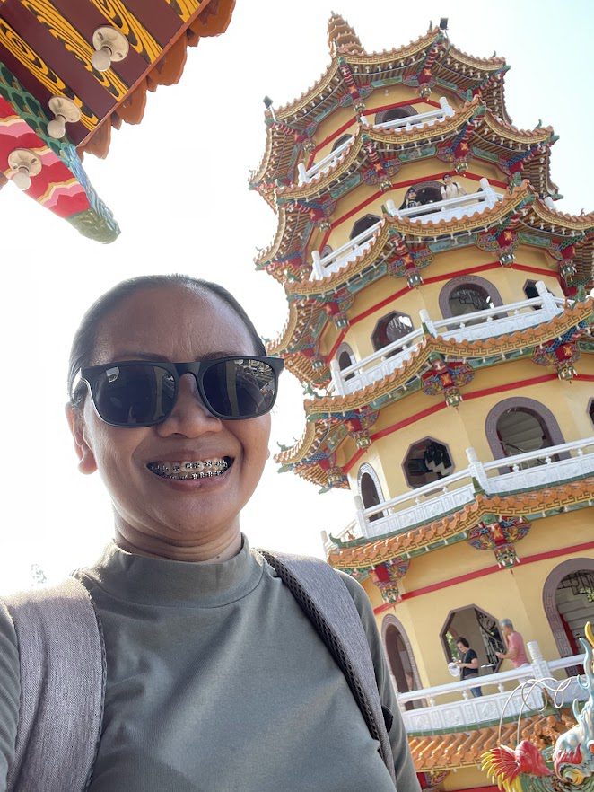 Portrait of a female traveler with a backpack smiling at the camera with a traditional Chinese pagoda in the background.